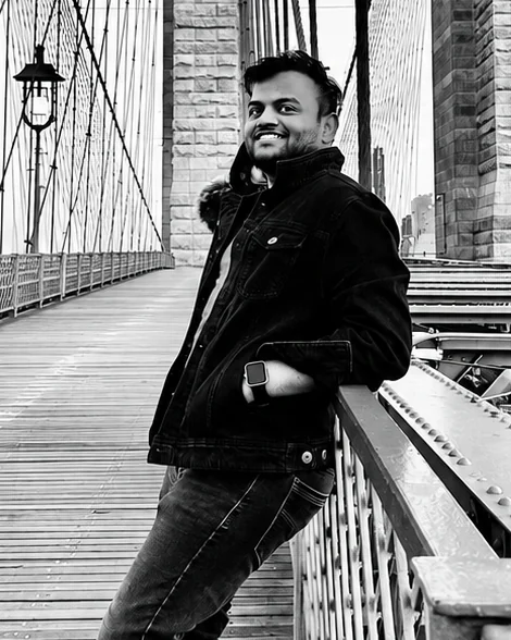 Girish Kumar Adari, leaning against the railing on the Brooklyn Bridge walkway.
